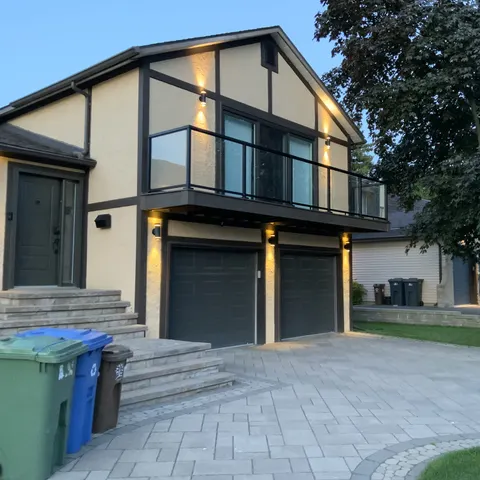 Balcon avec garde-corps en verre au-dessus d’un garage double, éclairage extérieur et entrée en pavés