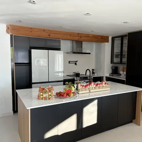Cuisine rénovée : armoires noires mates, îlot en quartz blanc, poutre de bois apparente et robinetterie noire
