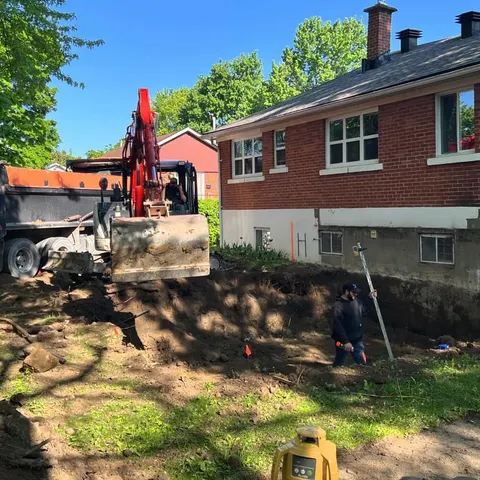 Excavator digging the foundation of a home addition behind a brick bungalow