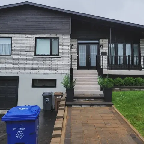 Façade de bungalow modernisée : revêtement noir, brique blanchie, portes doubles noires et garde-corps en aluminium