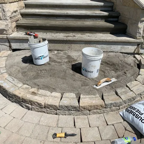 Marches de béton resurfacées et palier de pavés en cours devant une maison en pierre