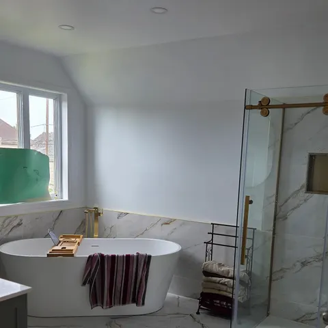 Salle de bain principale rénovée : bain autoportant, robinet sur pied en laiton brossé, douche vitrée et céramique effet marbre