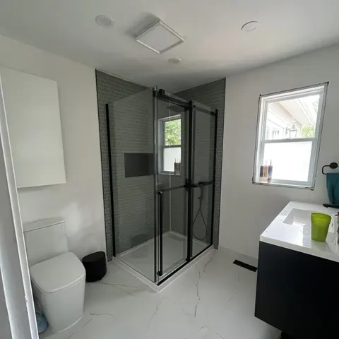 Salle de bain refaite : douche vitrée à cadre noir, céramique vert-de-gris et plancher effet marbre
