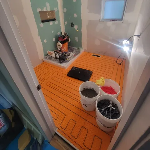 Salle de bain en chantier : membrane de plancher chauffant installée, base de douche et gypse hydrofuge