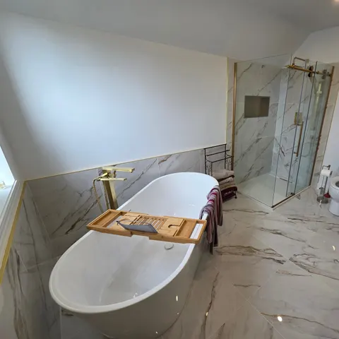 Salle de bain principale : bain autoportant, douche en verre à porte coulissante, niche encastrée et grands carreaux effet marbre