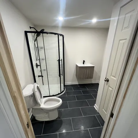 Salle de bain de sous-sol : douche en coin à cadre noir, céramique noire au sol et vanité flottante