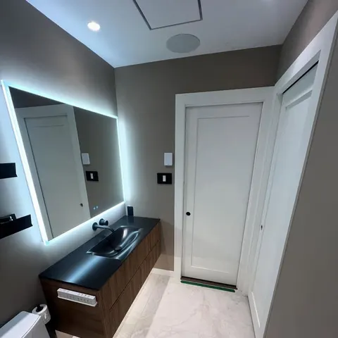 Renovated bathroom with floating walnut vanity, black sink and backlit mirror