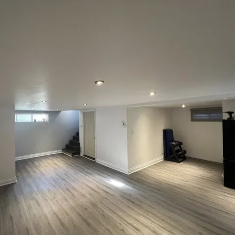 Sous-sol fini : plancher de vinyle gris, murs blancs, éclairage encastré et escalier
