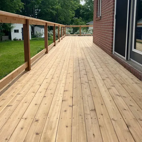 Plancher de terrasse en cèdre longeant une maison en brique, avec garde-corps en bois
